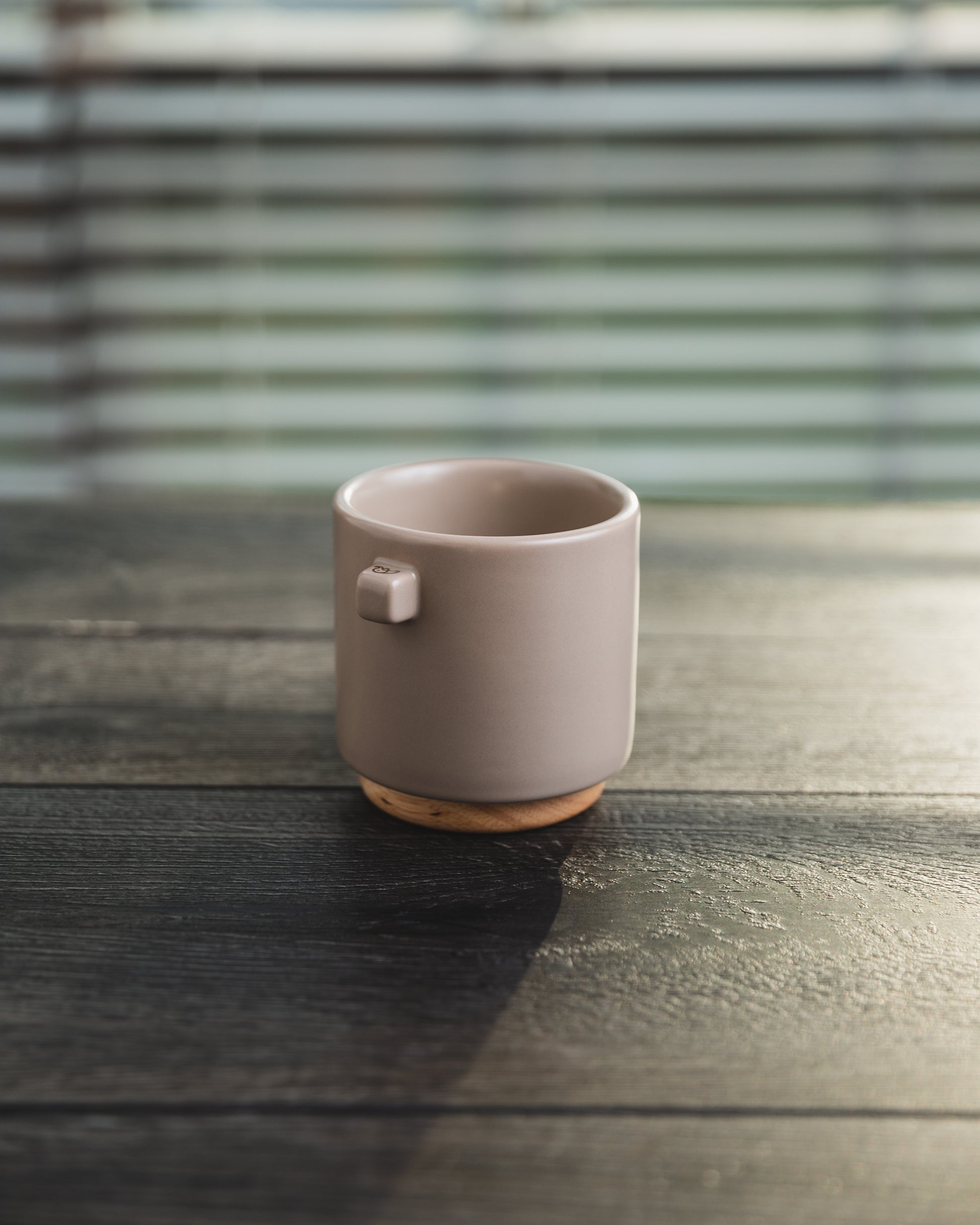 Upscale, ceramic, tuscan beige coffee mug with multiple key features. Built-in coaster, double wall, minimal handle for support, and spherical bottom for pouring. Made with high-quality ceramic and natural wood.