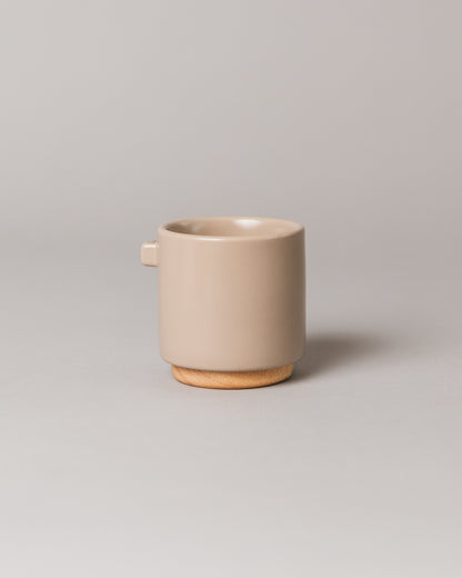 Upscale, ceramic, tuscan beige coffee mug with multiple key features. Built-in coaster, double wall, minimal handle for support, and spherical bottom for pouring. Made with high-quality ceramic and natural wood.