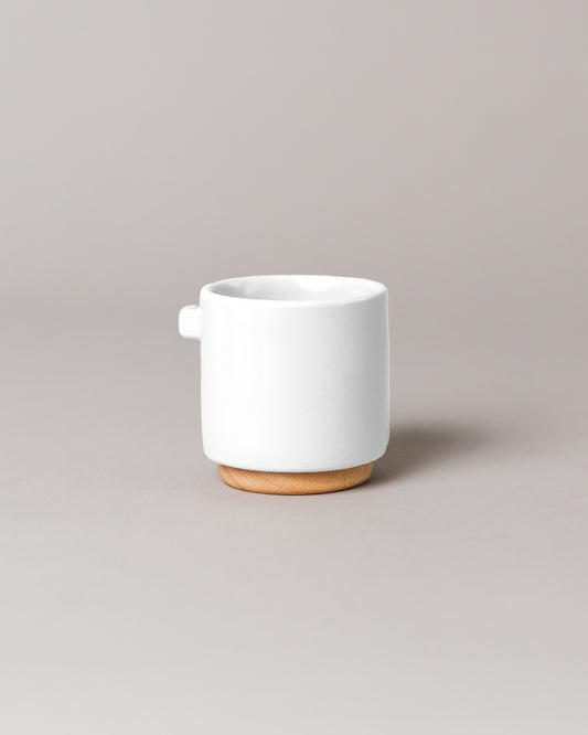 Upscale, ceramic, glacier white coffee mug with multiple key features. Built-in coaster, double wall, minimal handle for support, and spherical bottom for pouring. Made with high-quality ceramic and natural wood.