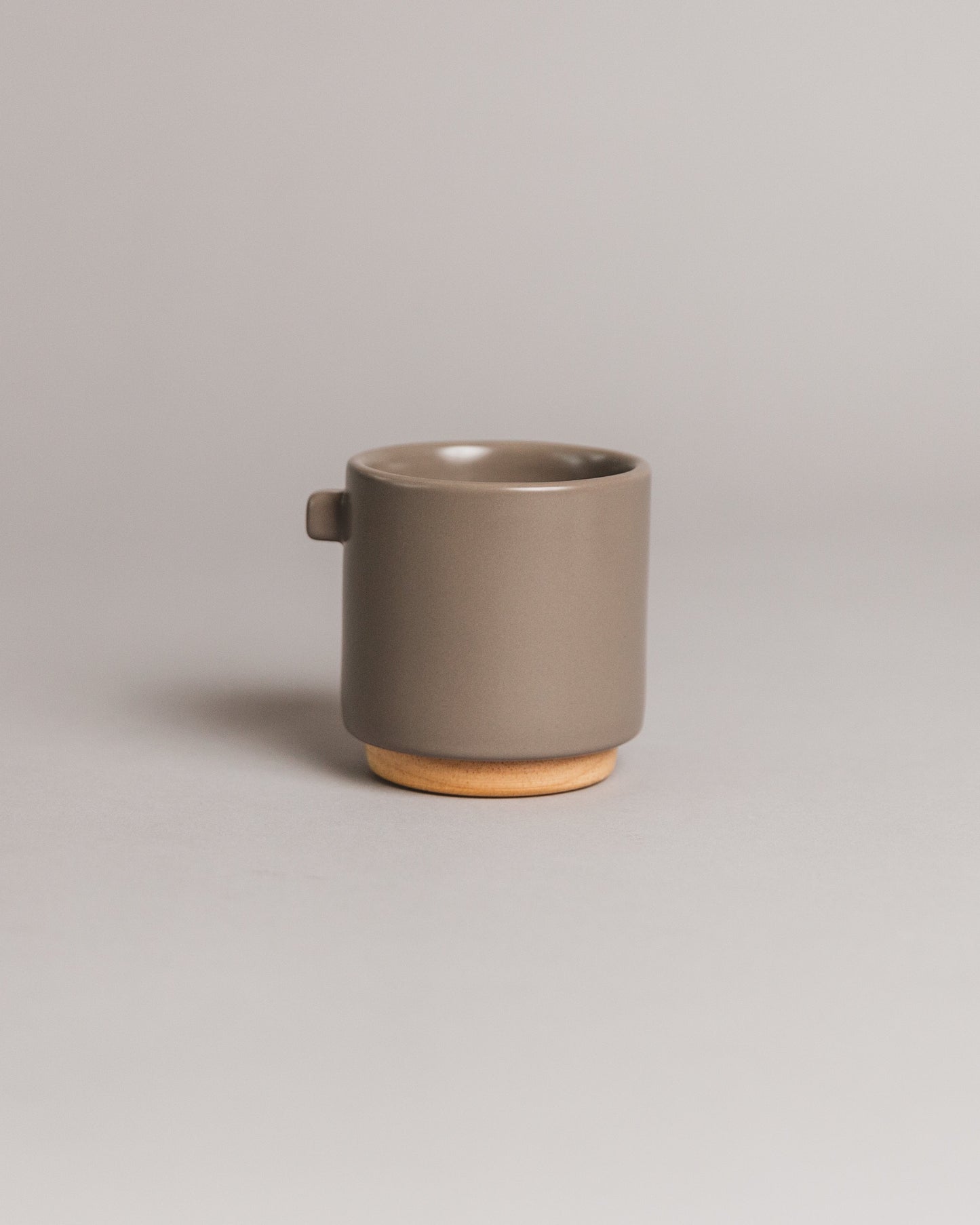 Upscale, ceramic, concrete grey coffee mug with multiple key features. Built-in coaster, double wall, minimal handle for support, and spherical bottom for pouring. Made with high-quality ceramic and natural wood. 